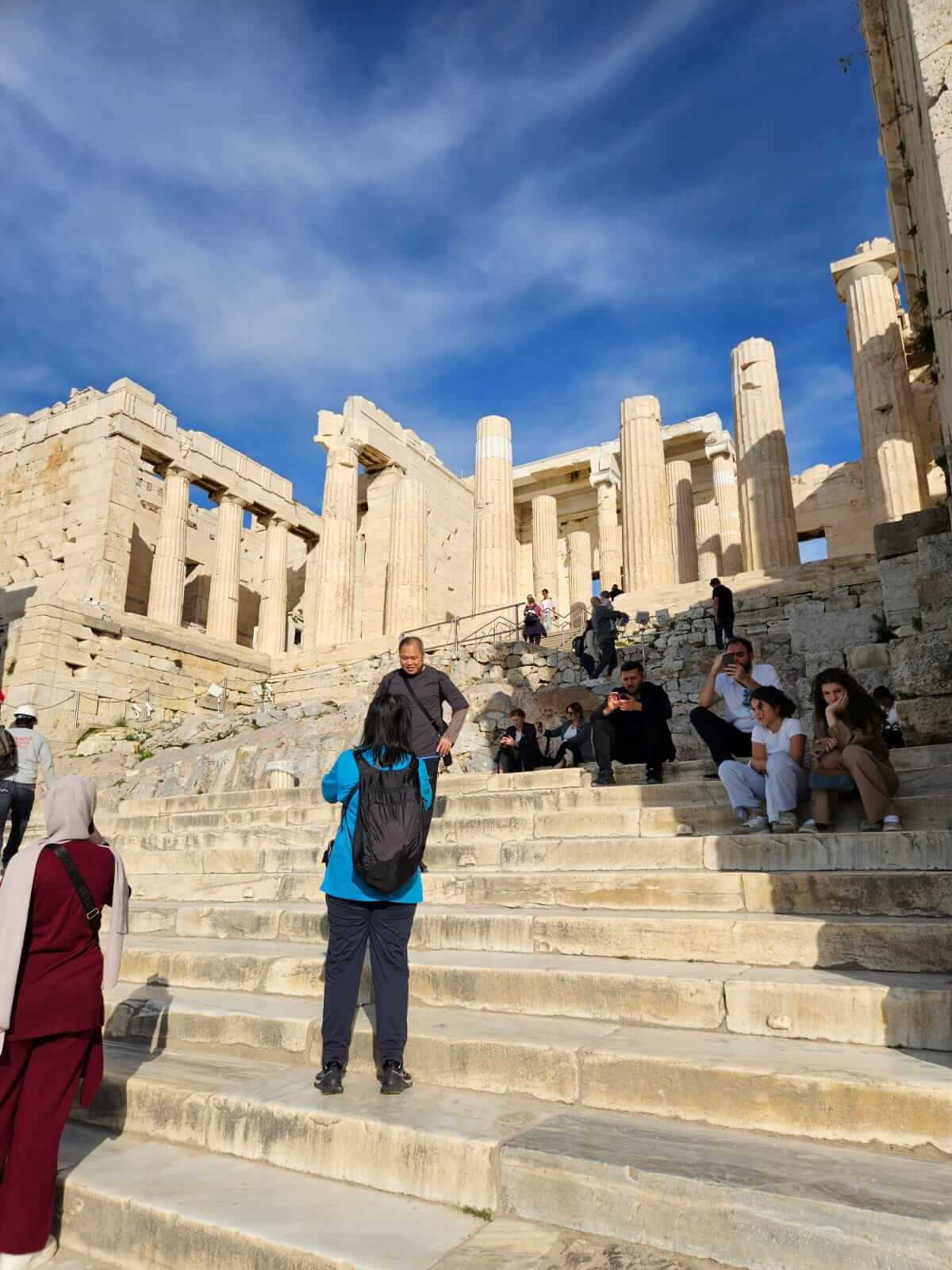 Touristen erkunden die antiken Ruinen bei sonnigem Himmel, während sie auf den historischen Steinstufen sitzen und posieren.